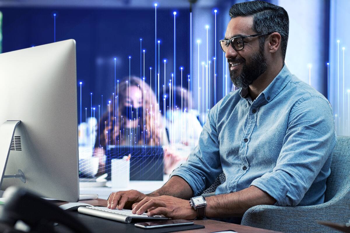 Male office worker happily typing away in front of his computer monitor. Blue data dots and lines pepper the surrounding.