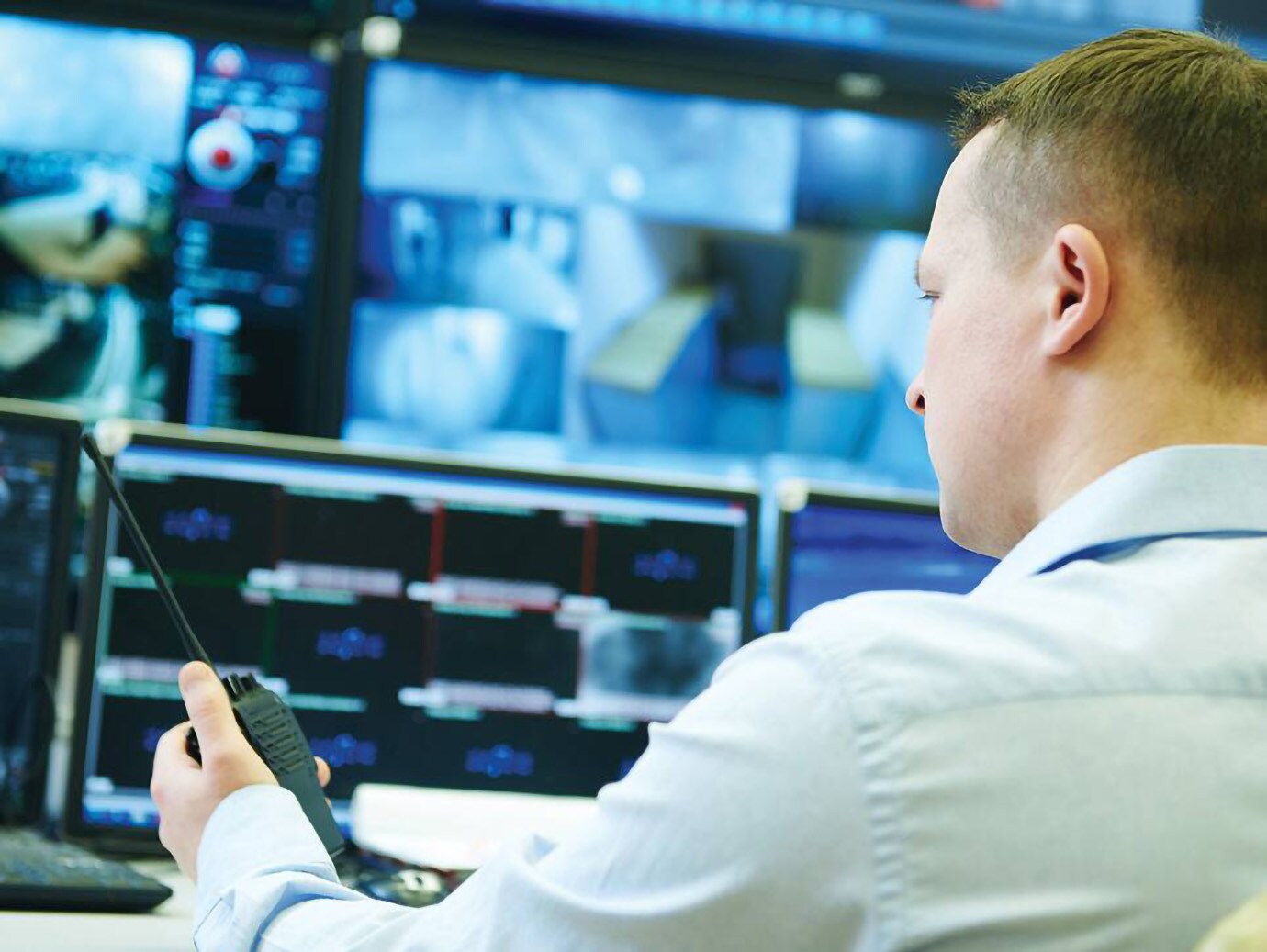 A person  holding a walkie talkie in his hand monitors the security cameras 
